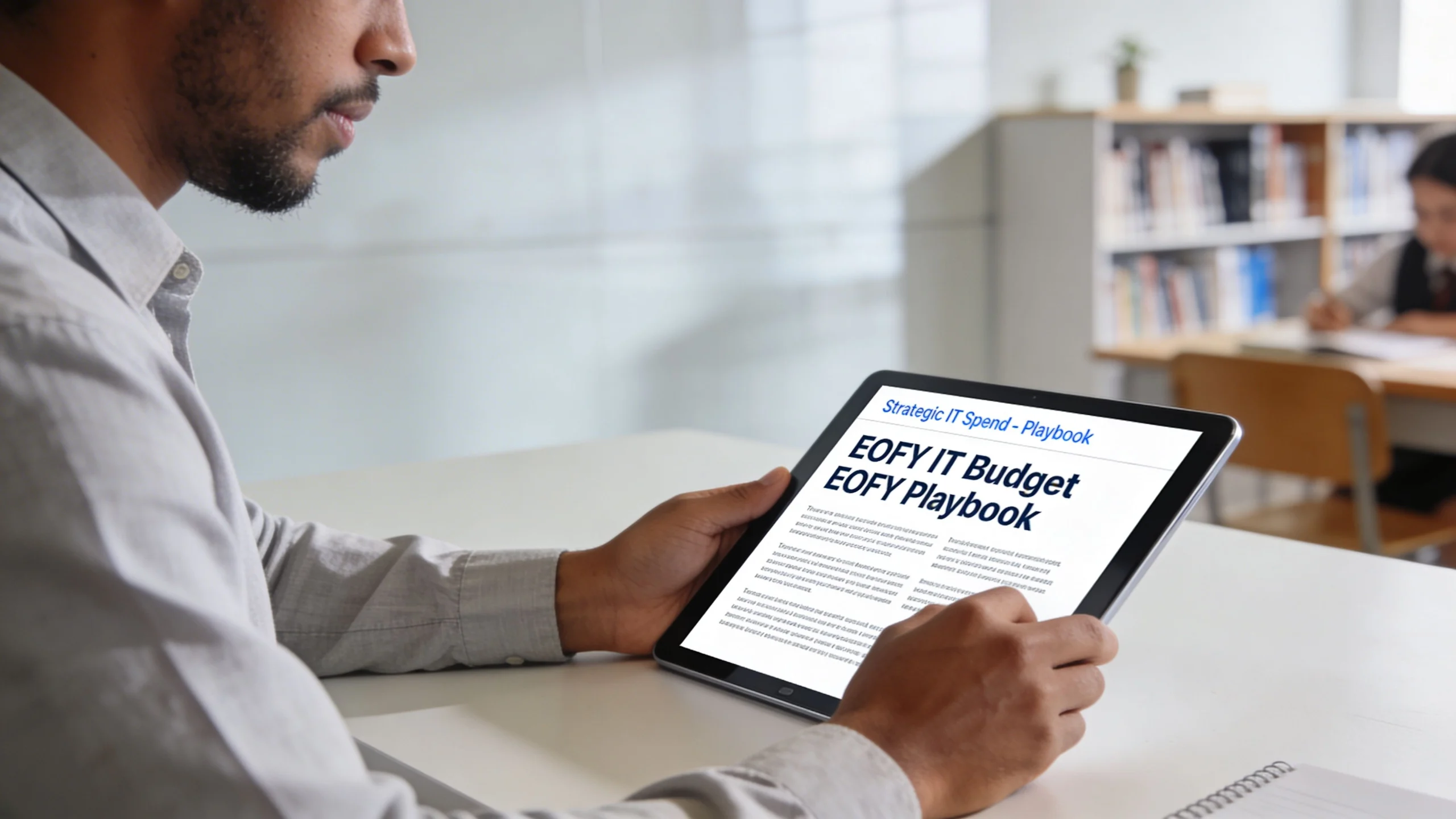A professional man holding a tablet while reading a strategic IT budget playbook in an office setting.
