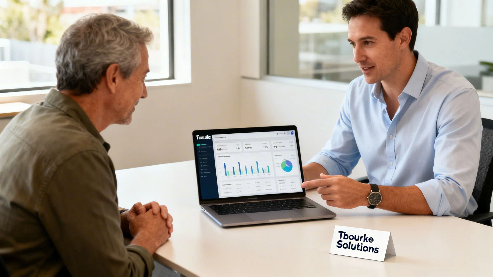Two men discuss data analytics on a laptop in an office, one pointing at charts.